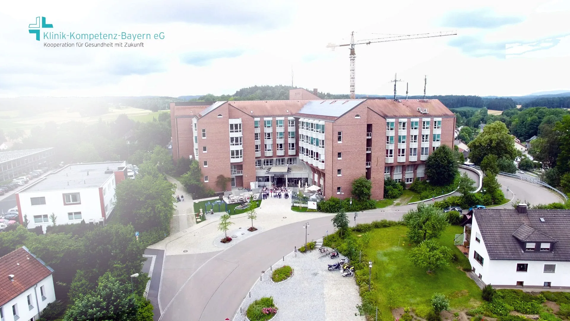 Still from the Klinik-Kompetenz-Bayern eG corporate film: aerial view of a clinic building with the cooperative’s logo